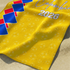 Diseño decorativo amarillo con patrón geométrico de rombos azules y rojos, texto "Virginia 2026 sutex towel closeup
