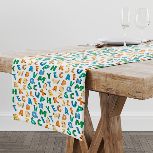 Patrón colorido de letras del alfabeto con diseños estilo dinosaurio en tonos azul, verde, amarillo y naranja sobre fondo blanco. table runner mockup