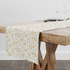 Patrón floral delicado con flores amarillas y hojas grises sobre rayas verticales en fondo crema table runner mockup