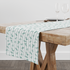 Patrón decorativo con rayas verticales y motivos florales de ramas verdes sobre fondo blanco table runner mockup