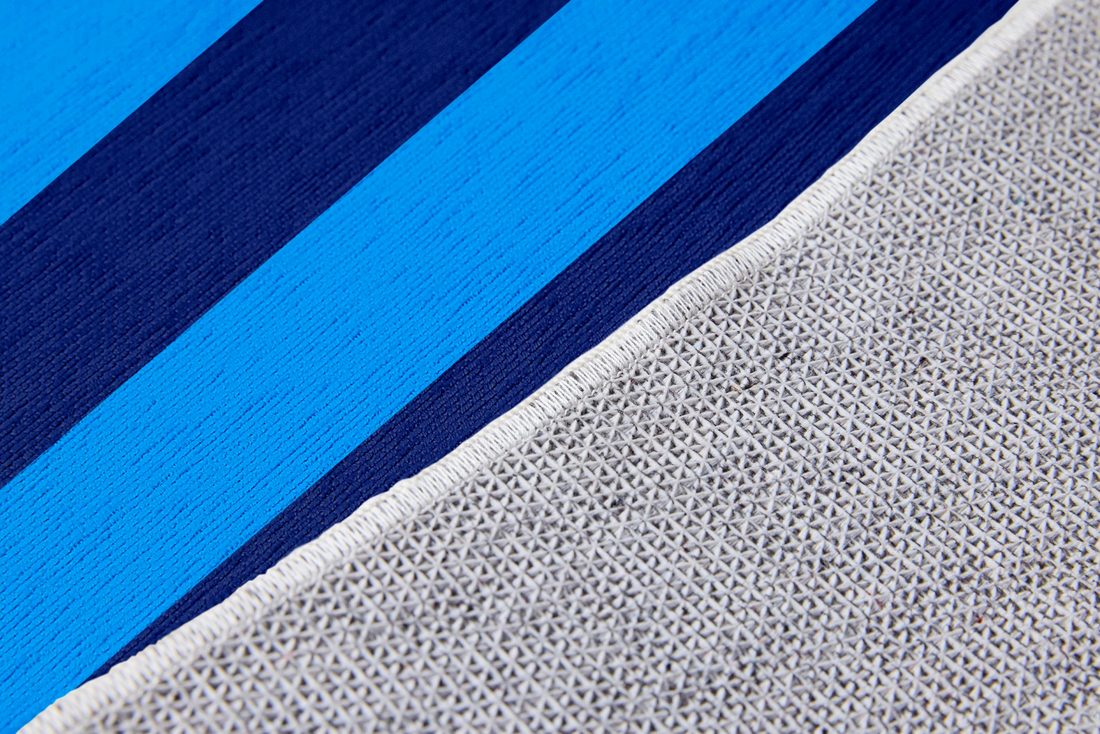Palabra "HOLA" en naranja sobre fondo de rayas verticales azules y azul marino sutex rug 2x3 closeup texture angled